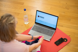 Eine Frau sitzt vor einem Laptop auf einer Gymnastikmatte.